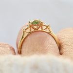 A close-up of an 18ct yellow gold engagement ring with a green oval sapphire worn on a finger.