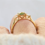 A close-up of an 18ct yellow gold engagement ring with a green oval sapphire worn on a finger.