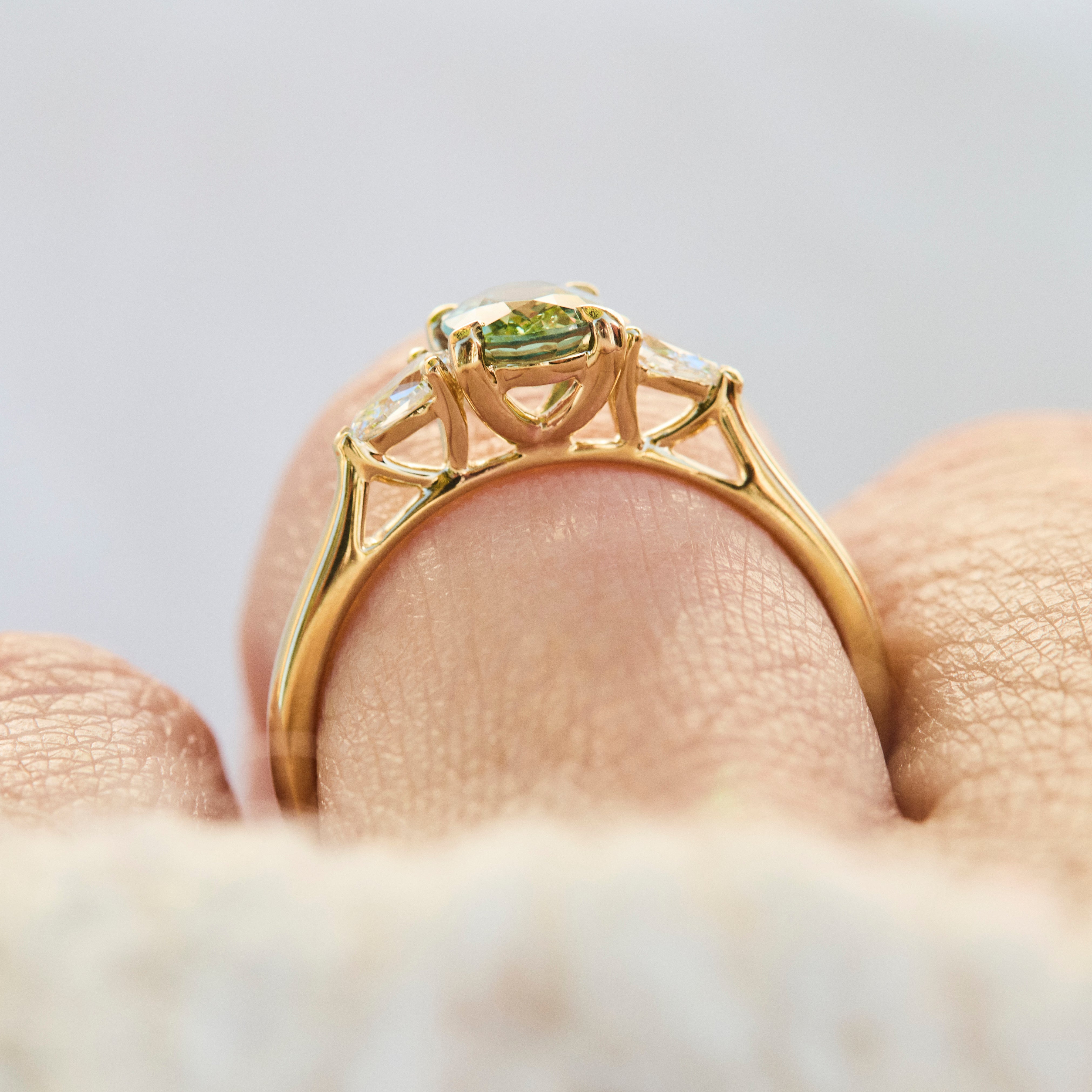 A close-up of an 18ct yellow gold engagement ring with a green oval sapphire worn on a finger.