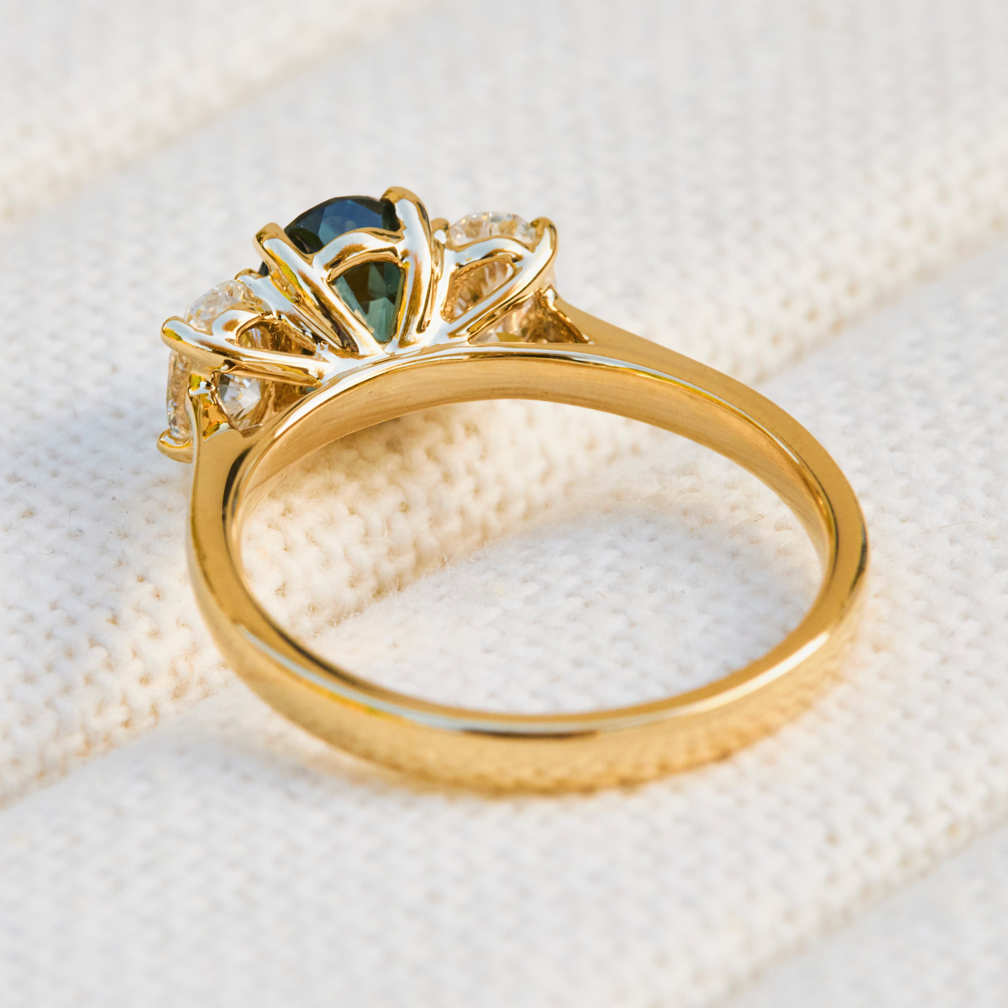 An 18ct yellow gold ring with a central teal sapphire and smaller clear accent lab grown side stones