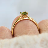 A close-up shot of an 18ct yellow gold engagement ring with a green oval sapphire.