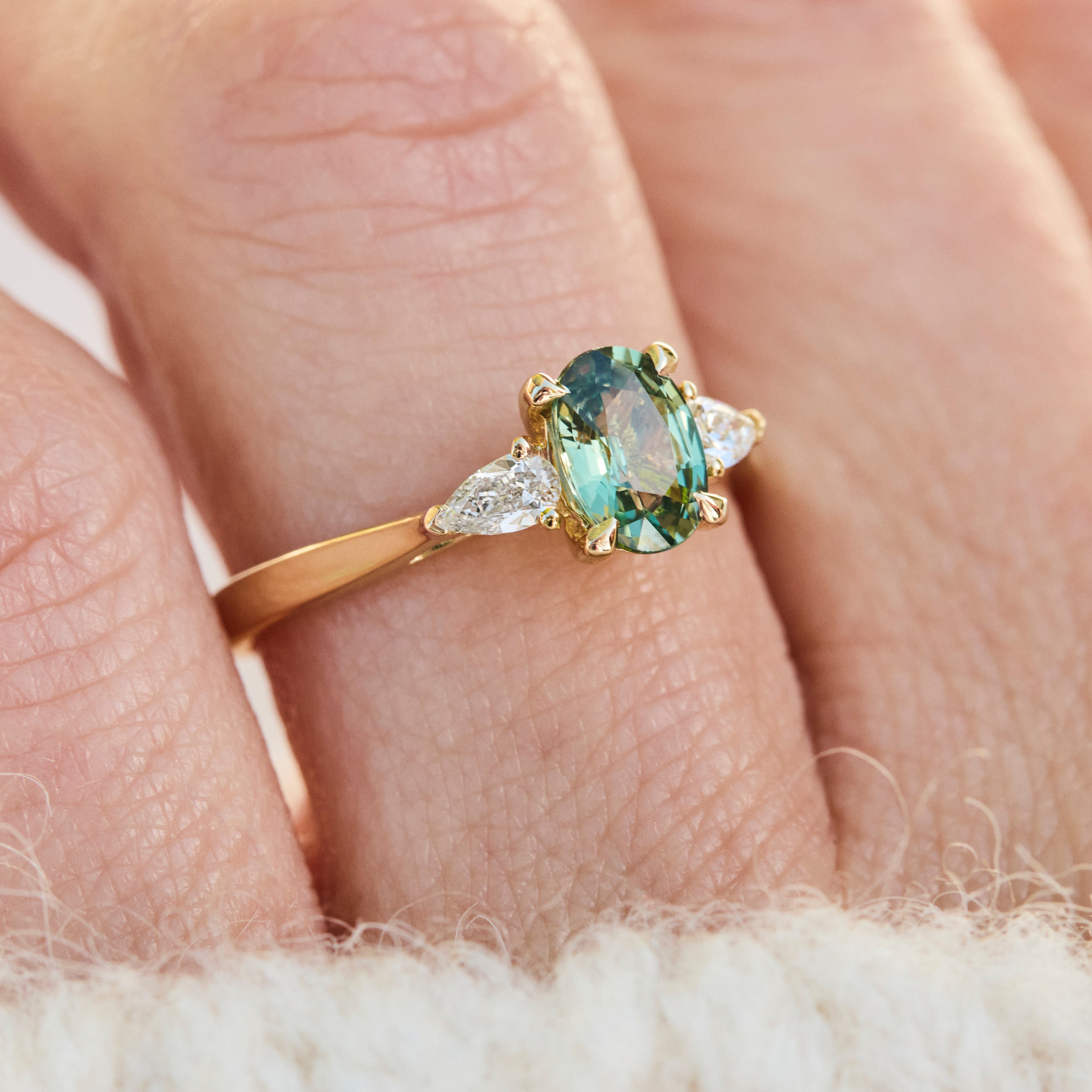 An 18ct gold engagement ring with an oval green sapphire and two pear shaped lab grown diamond side stones