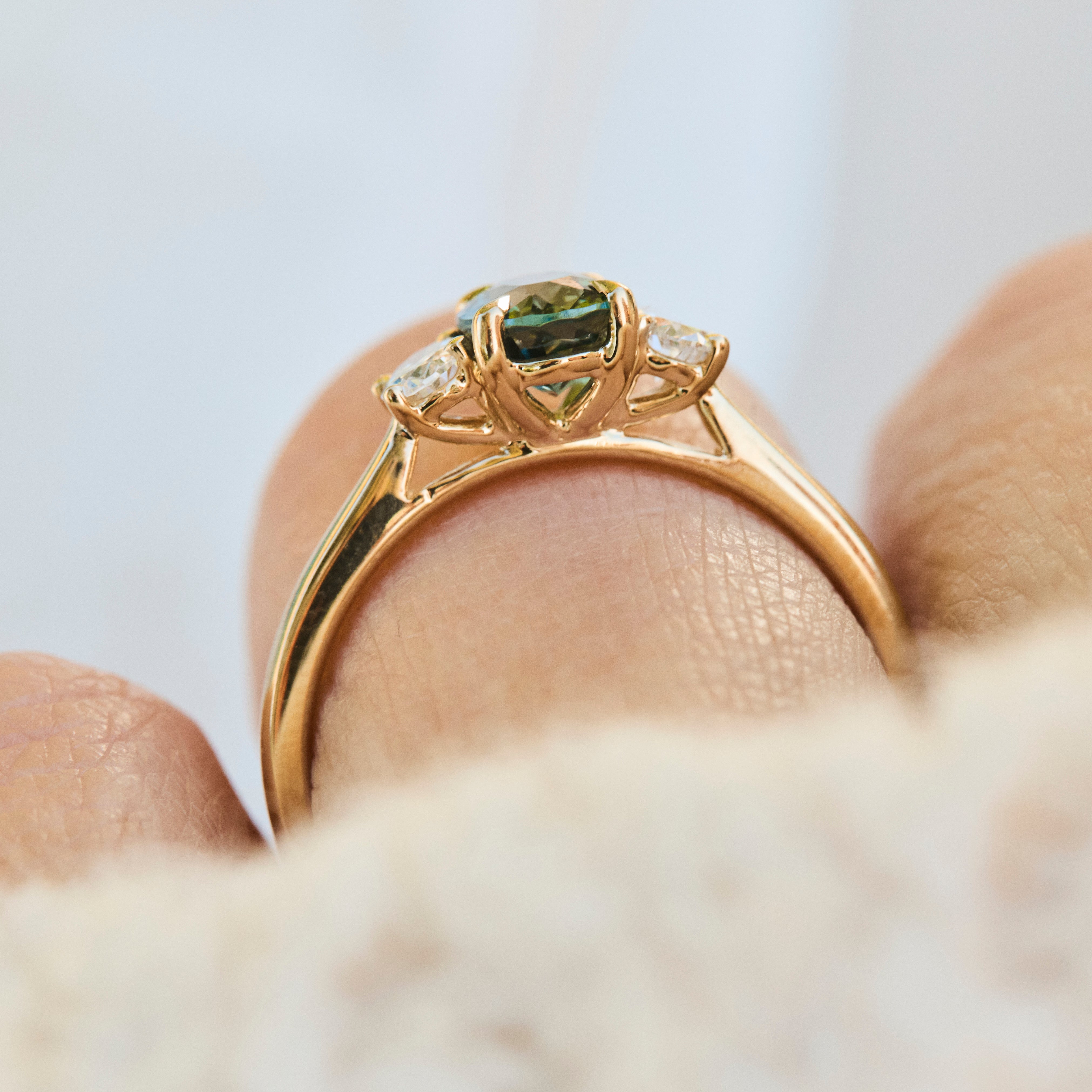A close-up of a yellow gold engagement ring with a green oval sapphire centre stone and small lab grown side stones.