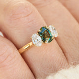 An 18ct yellow gold trilogy ring with a central oval-cut teal sapphire and two oval lab grown side diamonds.