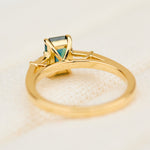 emerald cut teal sapphire trilogy engagement ring in yellow gold