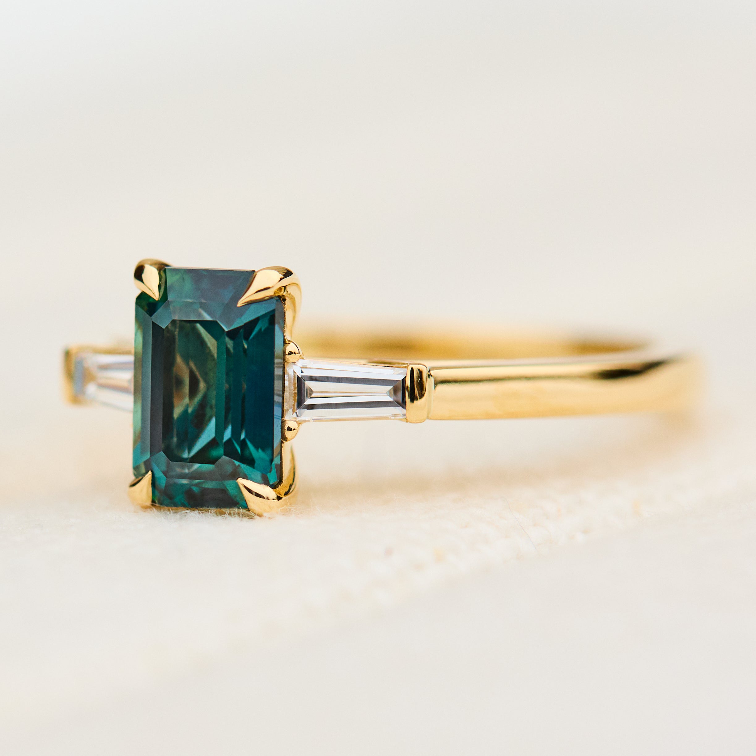 emerald cut teal sapphire trilogy engagement ring in yellow gold