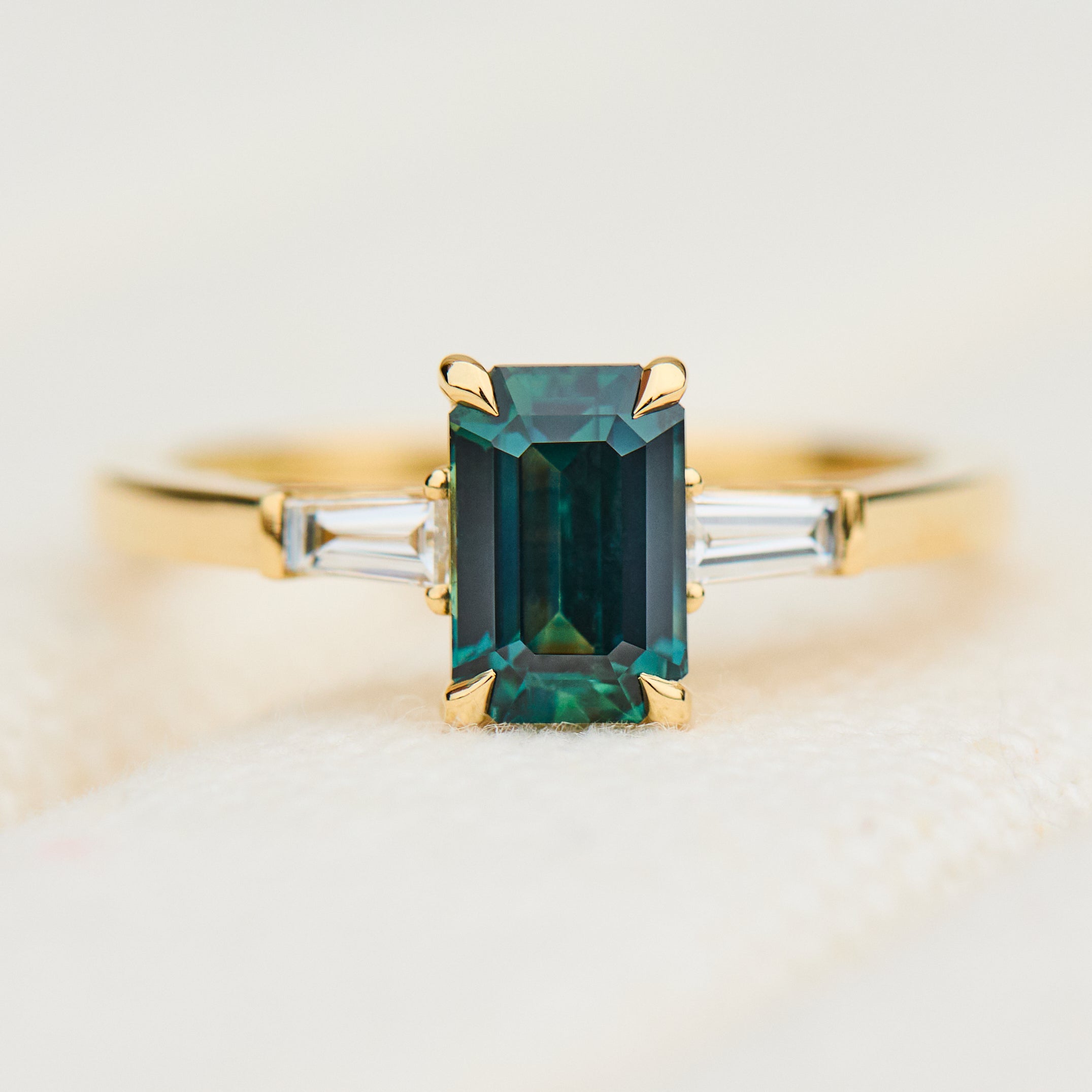 emerald cut teal sapphire trilogy engagement ring in yellow gold