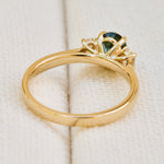 An 18ct yellow gold engagement ring with an oval teal sapphire  and smaller lab grown side diamonds.