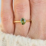 A close-up of an 18ct yellow gold ring with an oval green sapphire worn on a finger.