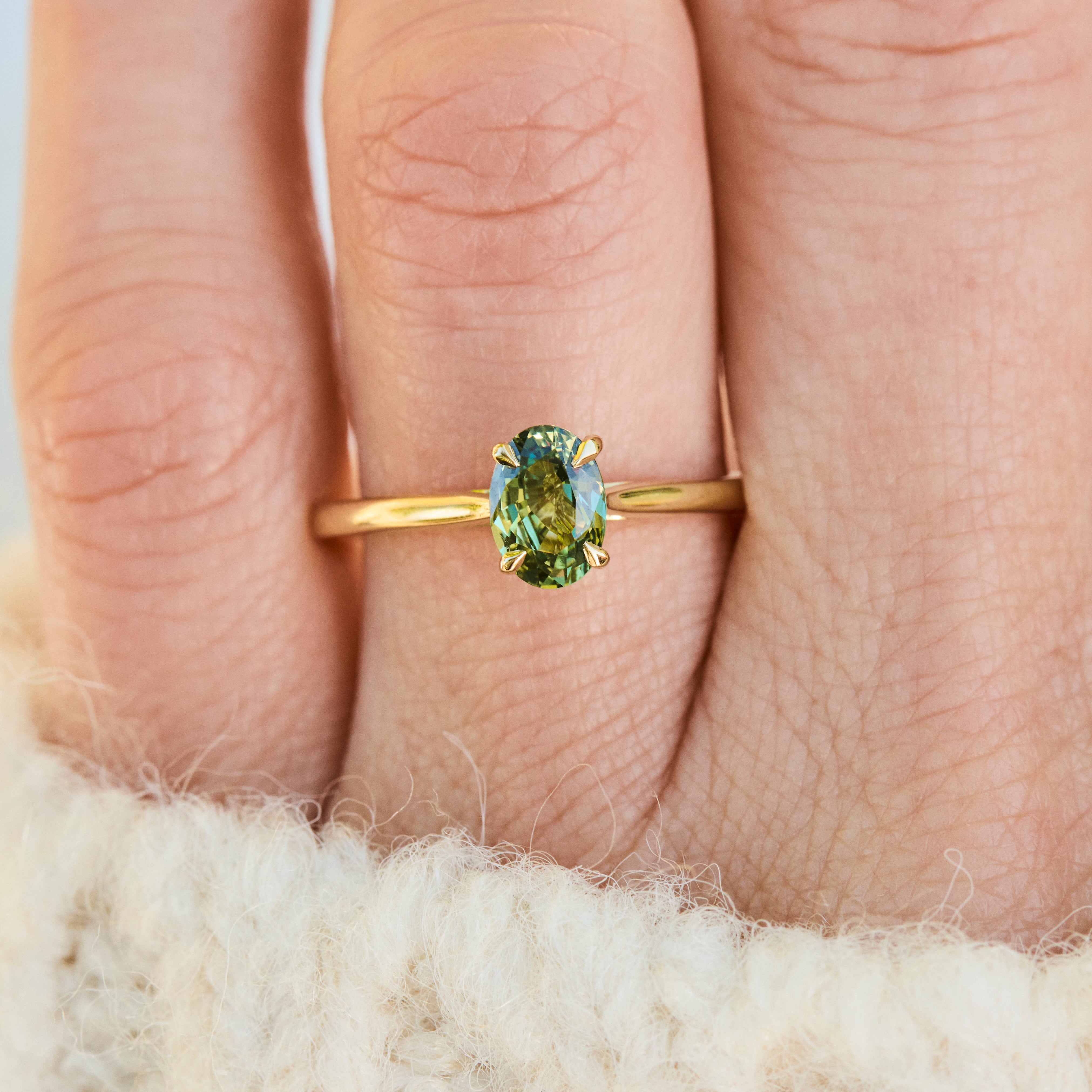 A close-up of an 18ct yellow gold ring with an oval green sapphire worn on a finger.