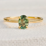 An 18ct yellow gold solitaire ring featuring an oval-cut green sapphire in a four-prong setting.