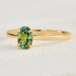 An 18ct yellow gold solitaire ring featuring an oval-cut green sapphire  in a prong setting.