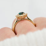oval teal montana sapphire engagement ring in yellow gold with a diamond halo