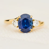 oval blue sapphire trilogy engagement ring in yellow gold paired with round side diamonds