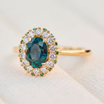 oval teal montana sapphire engagement ring in yellow gold with a diamond halo