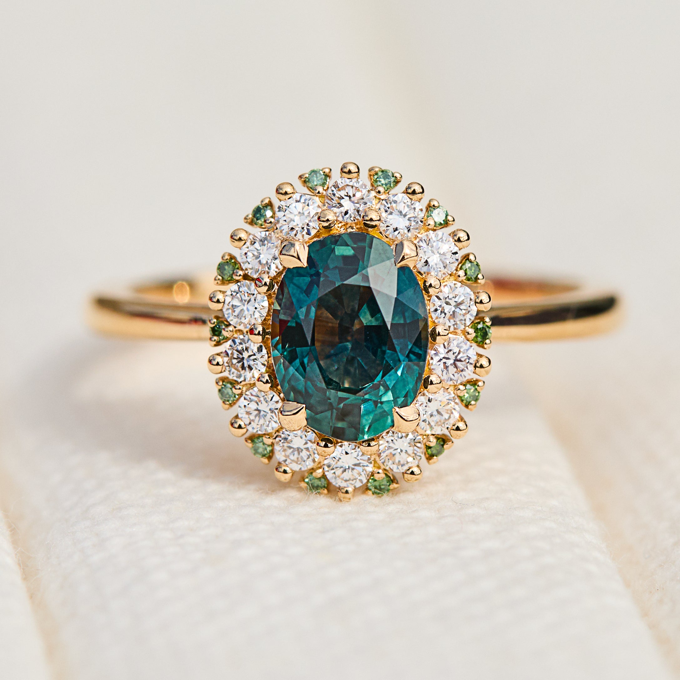 oval teal montana sapphire engagement ring in yellow gold with a diamond halo