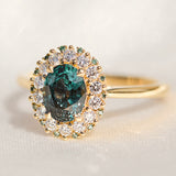 oval teal montana sapphire engagement ring in yellow gold with a diamond halo
