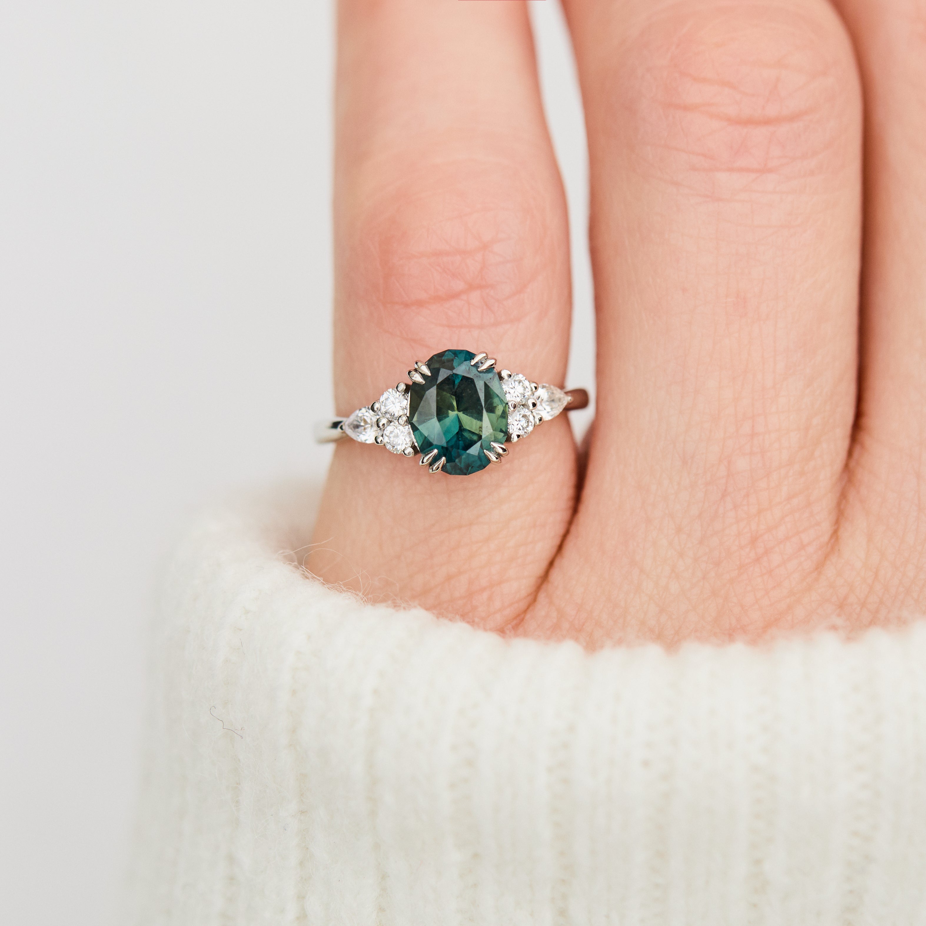 oval teal sapphire engagement ring set in platinum accented by six side diamonds