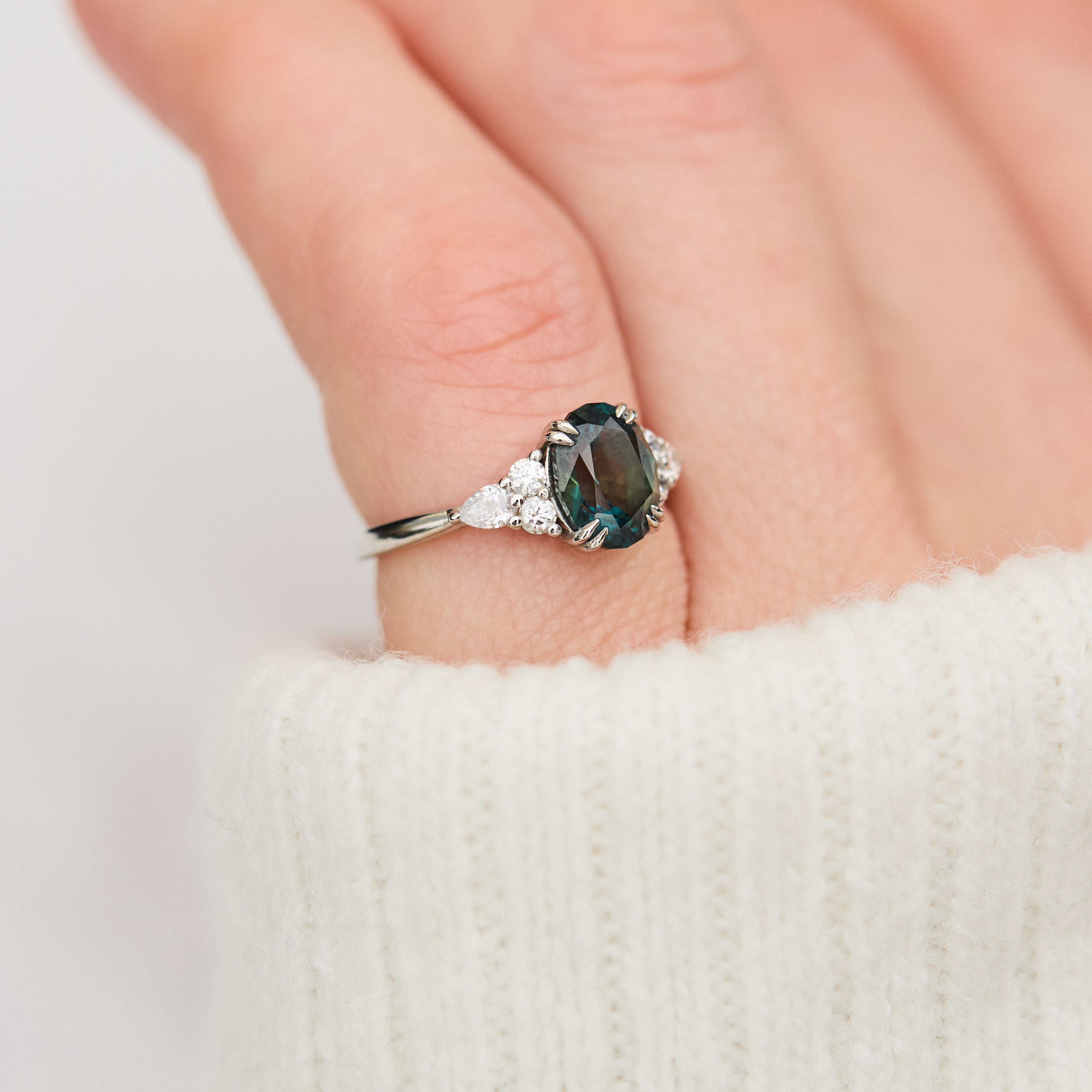 oval teal sapphire engagement ring set in platinum accented by six side diamonds