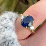 oval blue sapphire trilogy engagement ring in yellow gold paired with round side diamonds