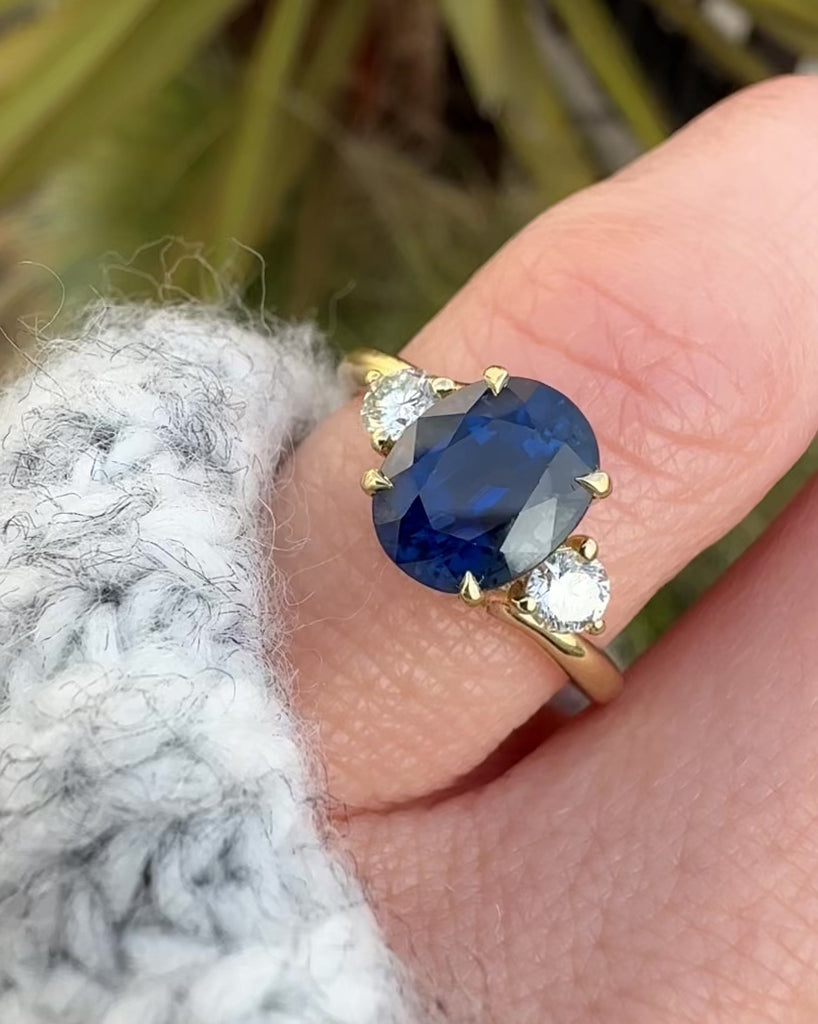 oval blue sapphire trilogy engagement ring in yellow gold paired with round side diamonds