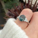 oval teal sapphire engagement ring set in platinum accented by six side diamonds