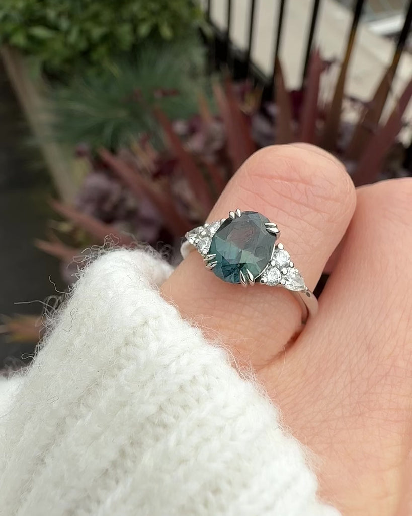 oval teal sapphire engagement ring set in platinum accented by six side diamonds