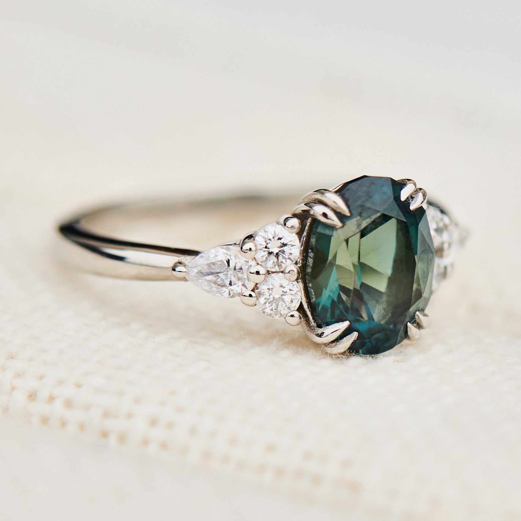 oval teal sapphire engagement ring set in platinum accented by six side diamonds